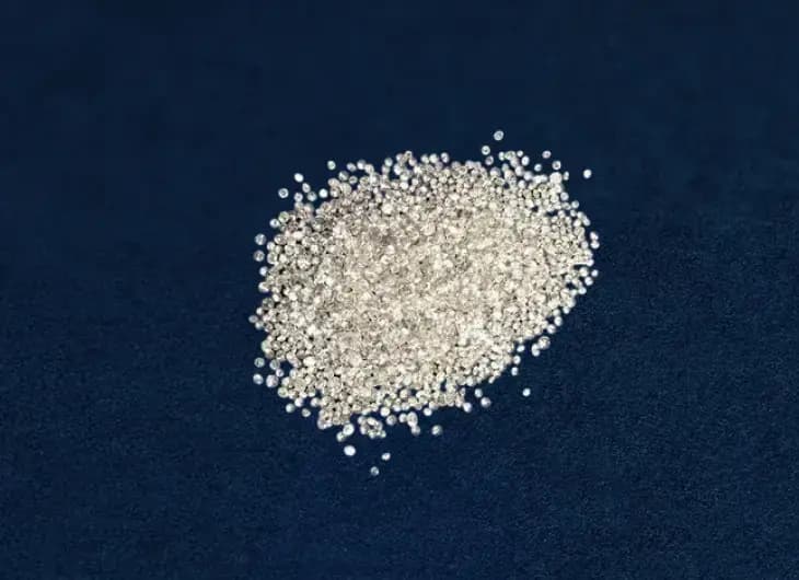 A pile of loose, sparkling small diamonds displayed against a deep navy blue background